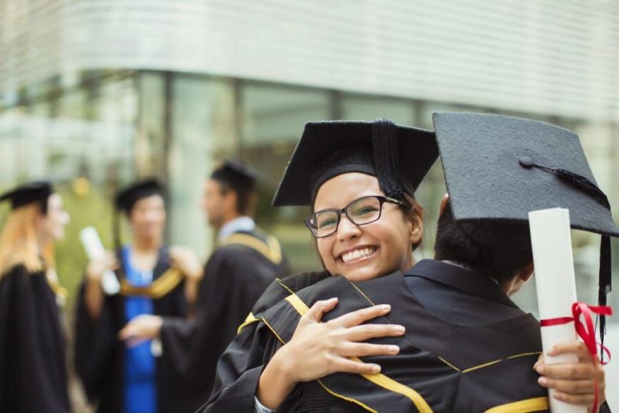 graduates in caps and gowns hugging